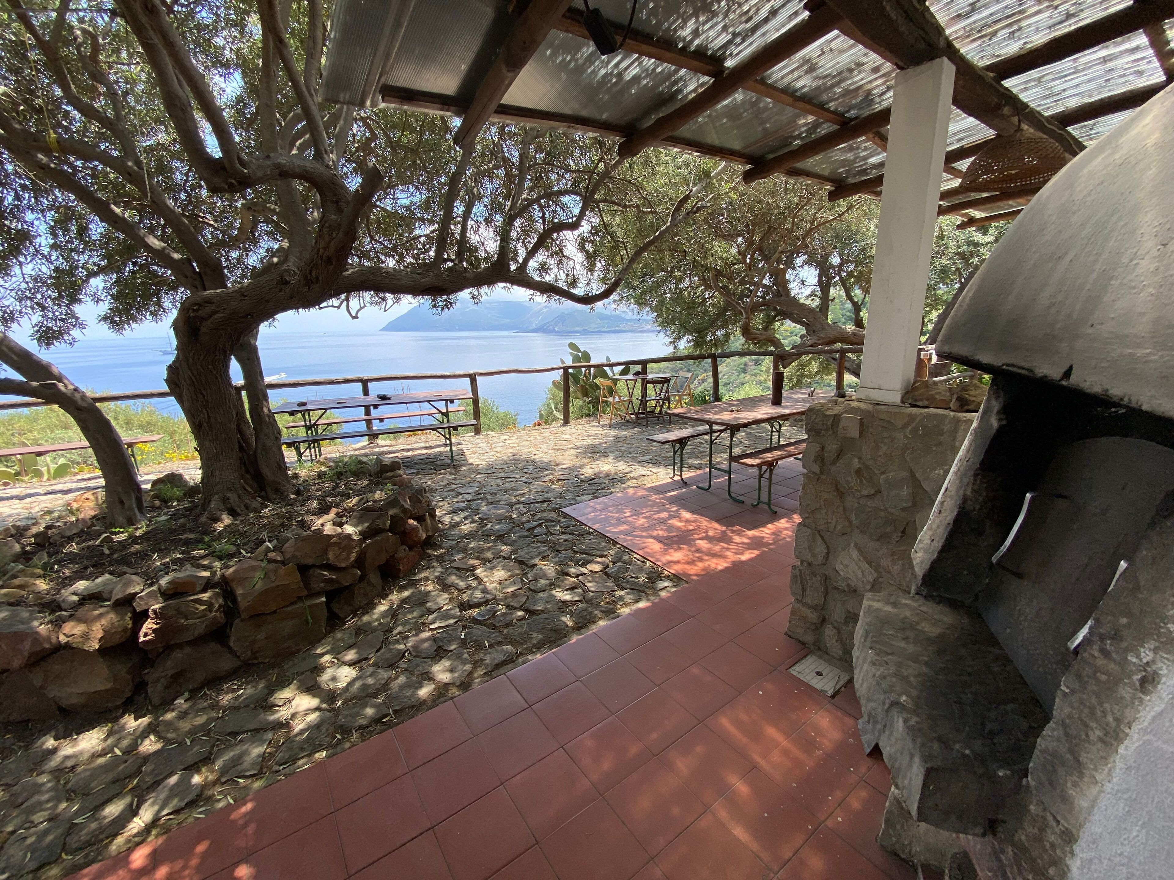 Un patio al aire libre con suelo de piedra, mesas de picnic, un muro de piedra y vistas al mar.