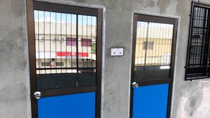 Dos puertas con barrotes metálicos y un panel azul, frente a una pared de concreto con un enchufe visible.