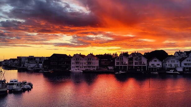 A waterfront property with a row of houses, a dock with boats, and a sunset sky. - Åkrehamn Marina (Karmoy)