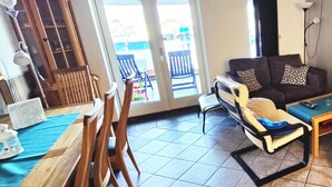 A living room with a dining area, a sofa set, a wooden cabinet, and a sliding glass door leading to an outdoor area. - Åkrehamn Marina (Karmoy)