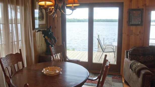 Un intérieur en bois comprenant une table à manger, des chaises, un canapé et une vue sur un lac, visible à travers une porte vitrée.