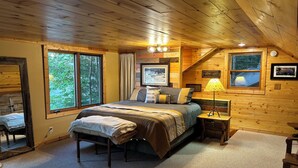 Une chambre confortable dans un chalet, avec un grand lit, une table de chevet, une lampe et une fenêtre donnant sur la forêt.