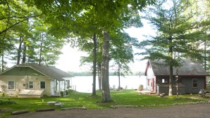 Un chalet au bord du lac, avec une cour gazonnée, un quai et un bateau.