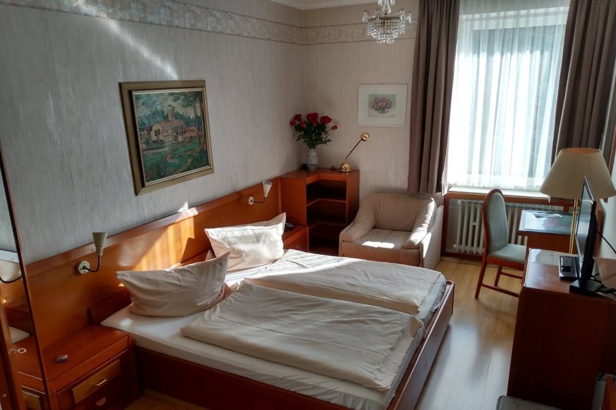 Een hotelkamer met een groot bed, een bureau, een stoel, een bijzettafeltje en een raam met gordijnen.