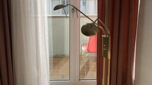 Una habitación con una lámpara de pie, un ventanal de vidrio a un balcón y cortinas.