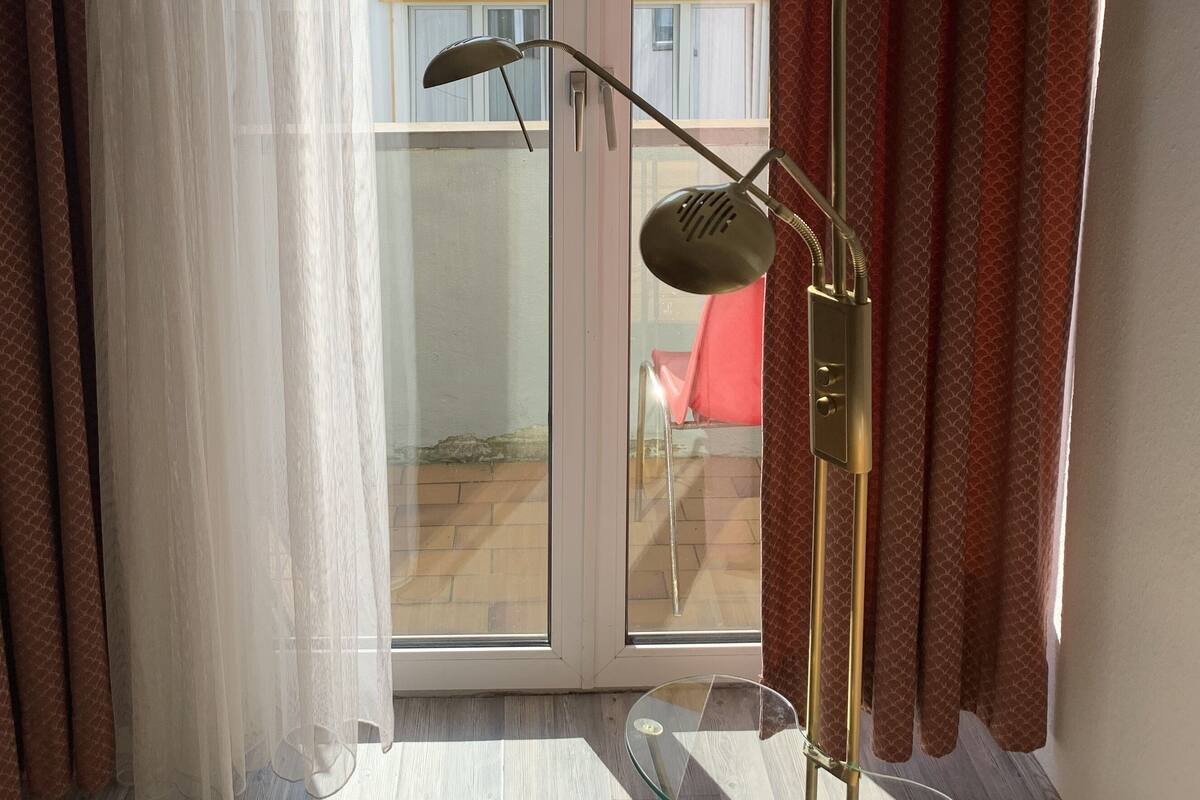 Een kamer met een vloerlamp, een glazen deur naar een balkon en gordijnen.