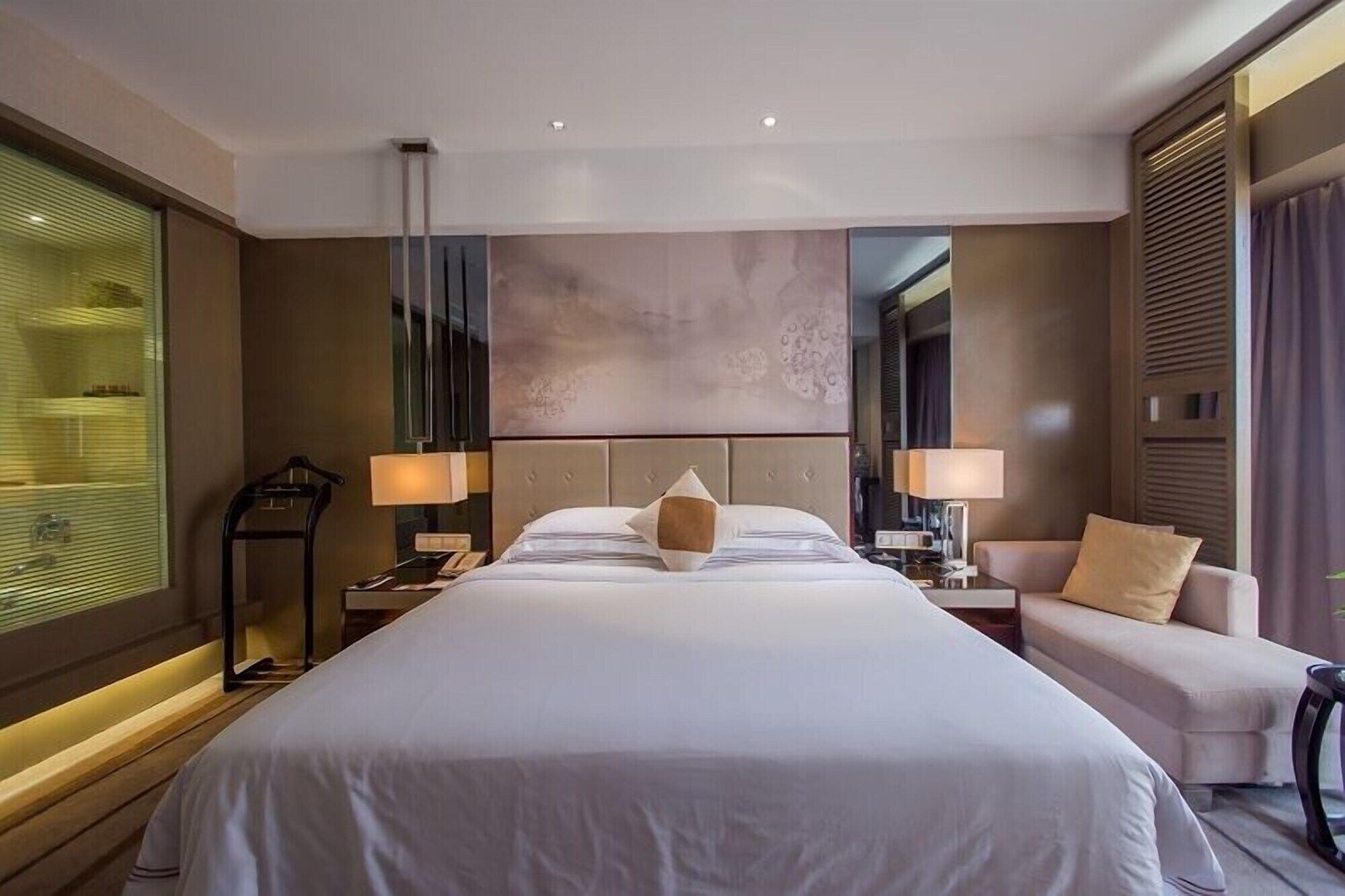 Una habitación de hotel moderna con una cama grande, lámparas de noche, un escritorio y un sofá.