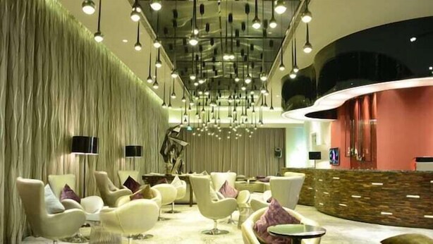 Eine moderne Lobby mit einer gebogenen Rezeption, komfortablen Sitzbereichen und einer hohen Decke mit Pendelleuchten.