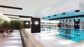Ein modernes Hallenbad mit gefliestem Boden, Liegestühlen und einer Decke mit Einbuchtungslichtern.