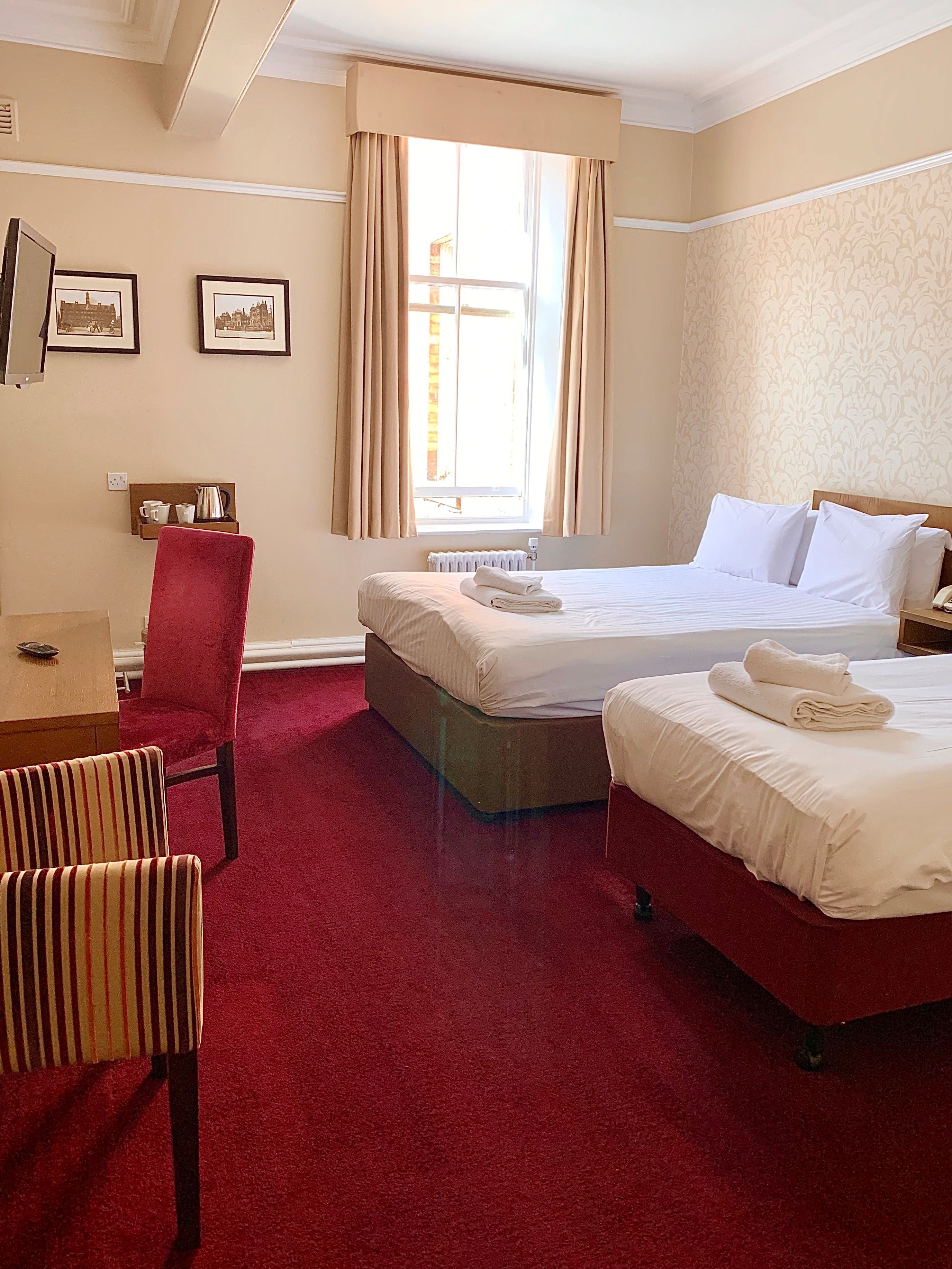 Habitación de hotel con dos camas, un escritorio, una silla y una ventana con cortinas.
