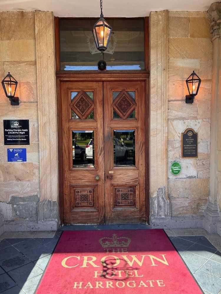 Una puerta doble de madera con una alfombra roja que conduce al Hotel Crown Harrogate.