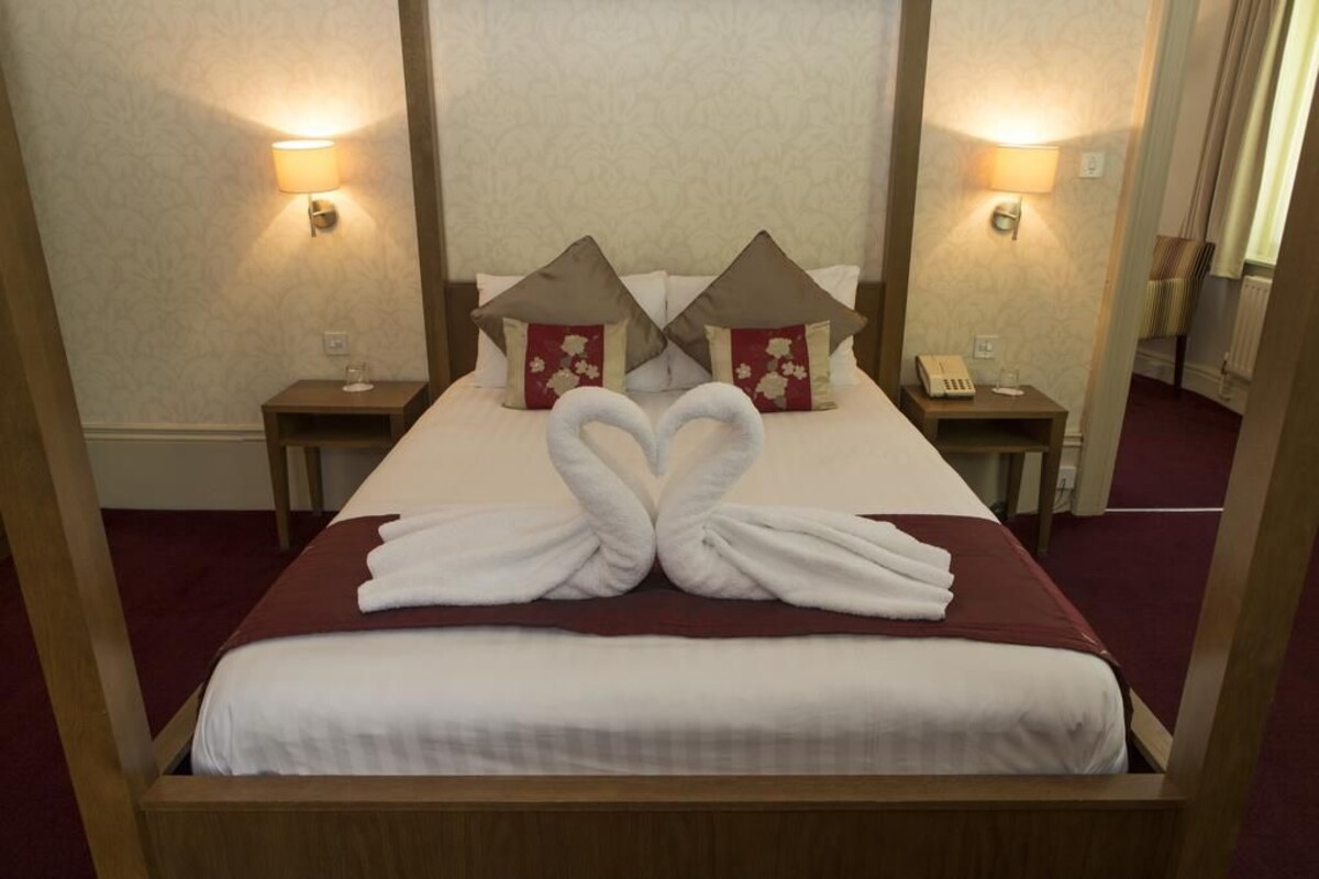 A neatly made bed with a red bedspread and two pillows, a bedside table with a lamp, and a telephone.