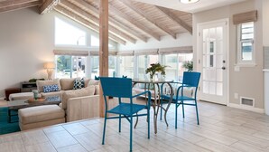 A spacious living room with a high ceiling, large windows, and a dining area with blue chairs. - 5227S -185027: 3  BR, 2  BA House in Oxnard, Sleeps 7 (Oxnard)