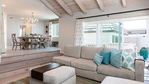 A spacious living room with a beige sofa, a coffee table, and a chandelier. A dining area with a wooden table and chairs is visible in the background. - 5227S -185027: 3  BR, 2  BA House in Oxnard, Sleeps 7 (Oxnard)