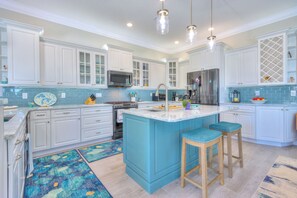 Une cuisine moderne avec des meubles blancs, un îlot central bleu, des appareils en acier inoxydable et des luminaires suspendus.