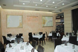 A restaurant interior with tables set for dining, a wine rack, and framed artwork on the walls. - Comfort (Tirana)