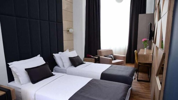 A hotel room with two beds, a desk, a chair, and a view of the outdoors. - Comfort (Tirana)