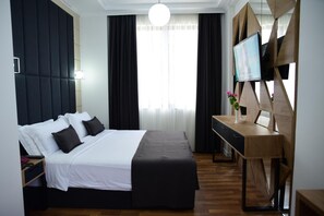 A hotel room with a bed, a desk, a television, and a window with curtains. - Comfort (Tirana)