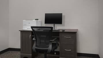 A hotel room with a desk, a chair, a flat-screen TV, a printer, and a filing cabinet.