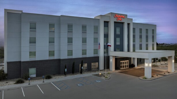 A Hampton Inn hotel with a modern facade, a covered entrance, and handicap-accessible parking.