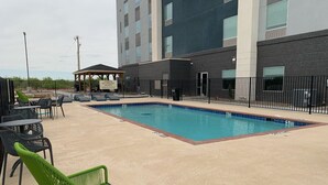 A pool area with lounge chairs and tables, a covered seating area, and a building with multiple windows.