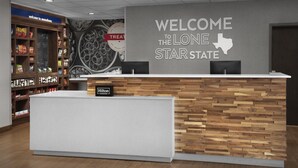Un espace d’accueil avec un comptoir en bois, une enseigne murale indiquant « BIENVENUE DANS L’ÉTAT DE LONE STAR », et des étagères remplies de collations et de boissons.
