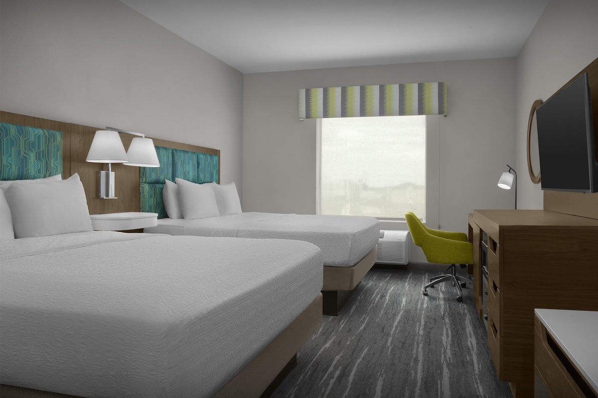 A hotel room with two beds, a desk, a chair, a TV, and a window with a view.