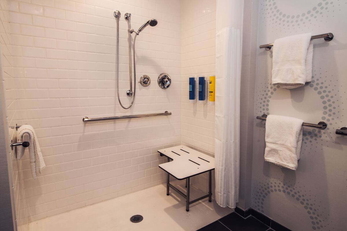 Ein modernes Badezimmer mit Dusche, Haltegriffen, einem kleinen Tisch und Handtuchhaltern.