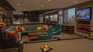Une table de billard avec un porte-billes, un canapé modulable avec plusieurs coussins et un téléviseur diffusant une publicité incitant au vote.