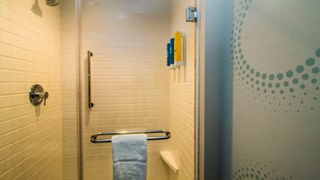 A shower with a glass door, a towel rack, and toiletries on the wall.