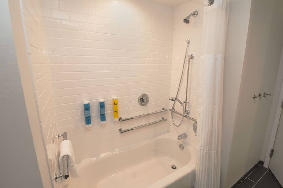 Ein modernes Badezimmer mit weißen Fliesen, einer Badewanne, einer Dusche mit Glastür und Handläufen.