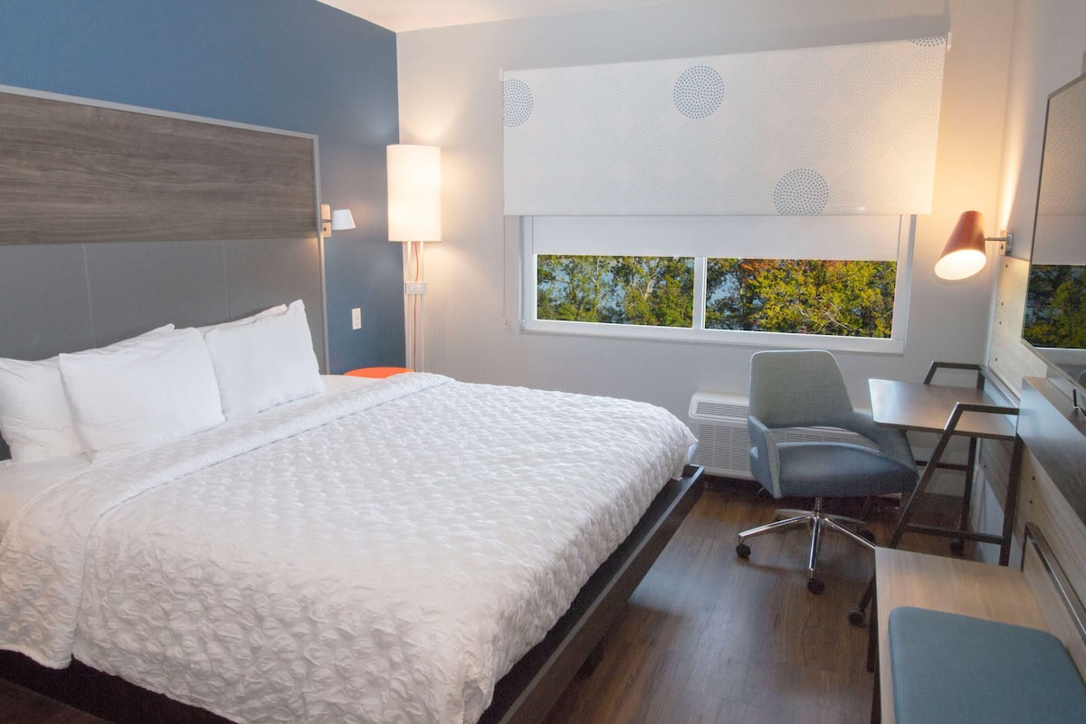 Ein Hotelzimmer mit einem großen Bett, einem Schreibtisch, einem Sessel und einem Fenster mit Blick auf Bäume.