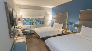 Une chambre d’hôtel avec deux lits, un bureau, une chaise et une fenêtre donnant sur des arbres.
