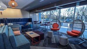 Un espace de détente moderne avec un canapé bleu, des fauteuils rouges et un coin salon agrémenté d’un tapis à motifs.