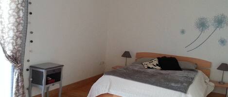 A bedroom with a wooden bed, a small bedside table, a chair, and a wall with a dandelion decoration.