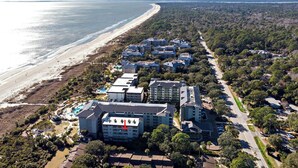 Ein Luftbild eines Küstenhotels mit mehreren Gebäuden, einem Strand und einer Straße.