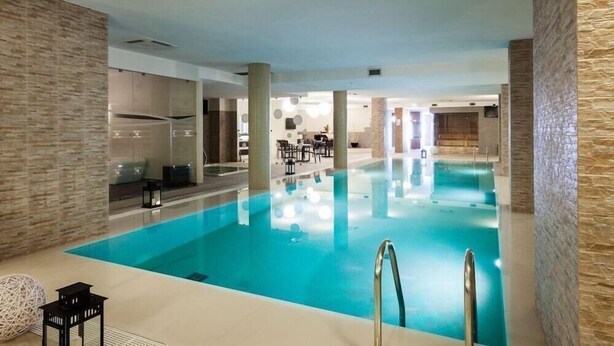 An indoor swimming pool with clear water, surrounded by stone walls and a seating area with tables and chairs. - Borgo Don Chisciotte (Modica)