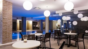 A modern indoor pool area with multiple seating arrangements and a visible swimming pool. - Borgo Don Chisciotte (Modica)