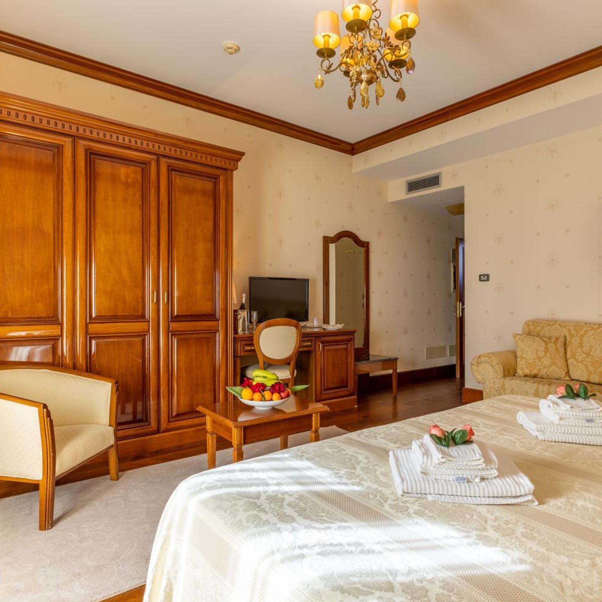 Een hotelkamer met een grote kast, een televisie, een spiegel, een bank en een bed met handdoeken.