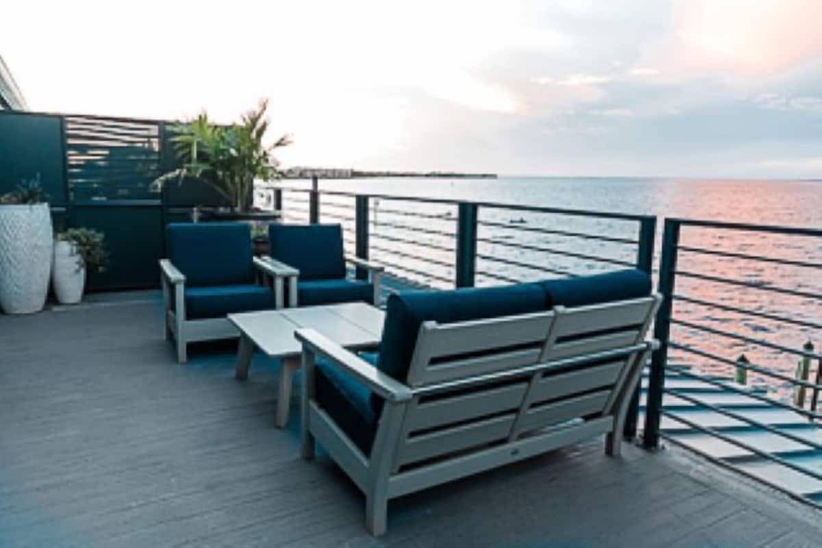A deck with outdoor seating, a railing, and a view of the sea.