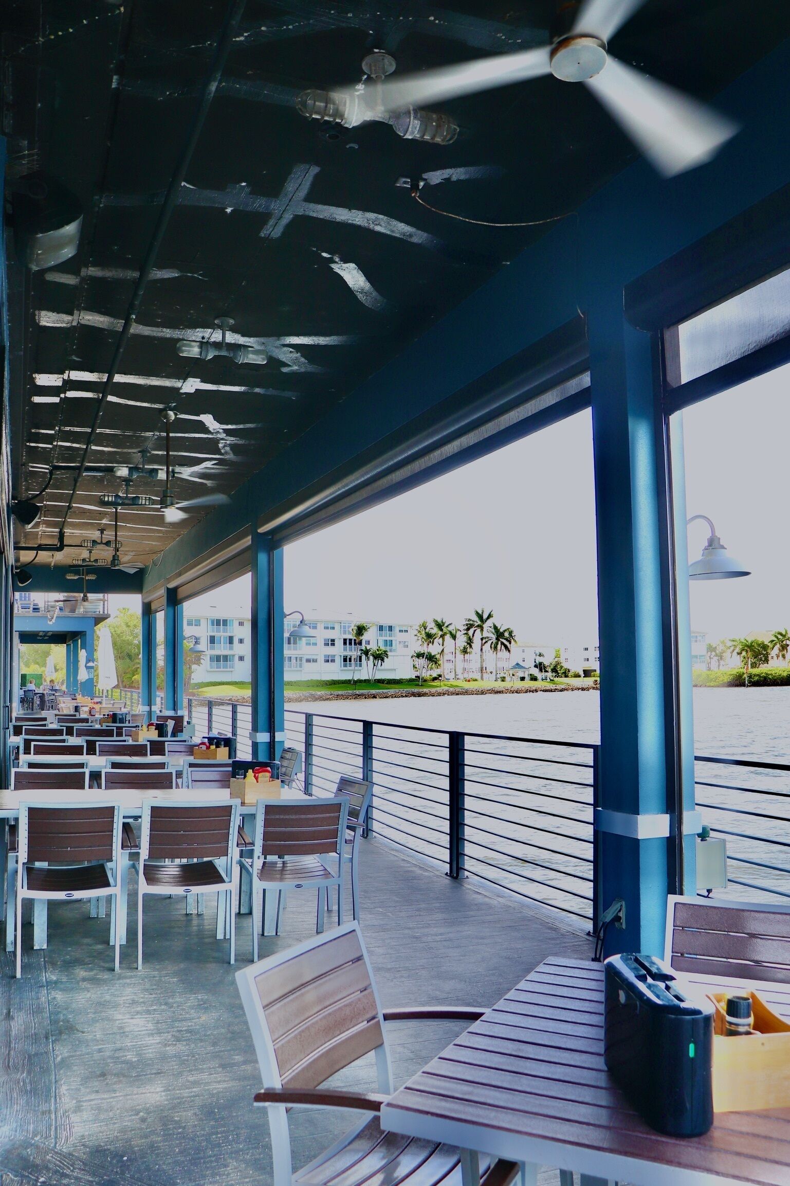 An outdoor seating area with tables and chairs, a view of a body of water, and a building in the background.