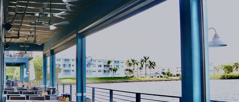 An outdoor seating area with tables and chairs, a view of a body of water, and a building in the background.