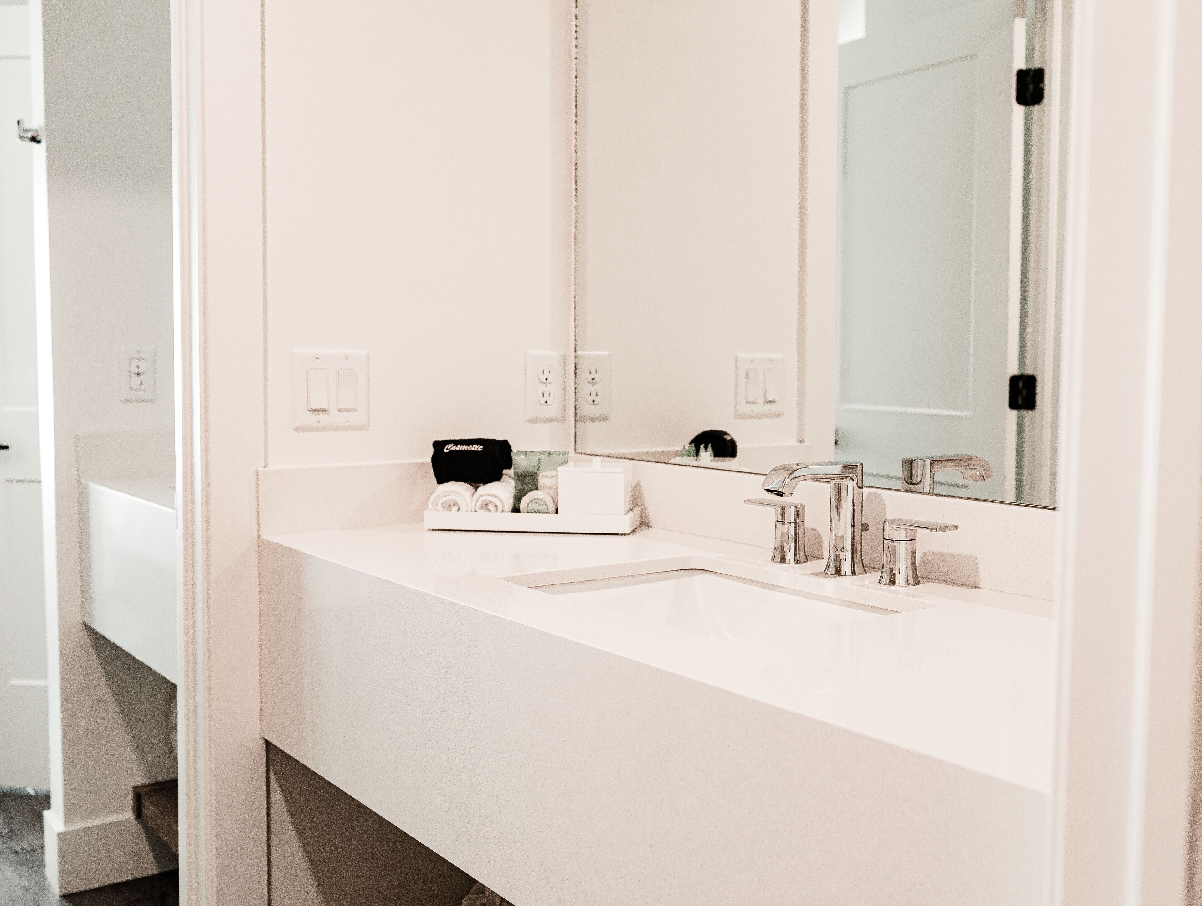 A modern bathroom with a white countertop, two sinks, and a large mirror.