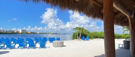A beach area with a thatched roof structure, blue chairs, and a view of the sea.