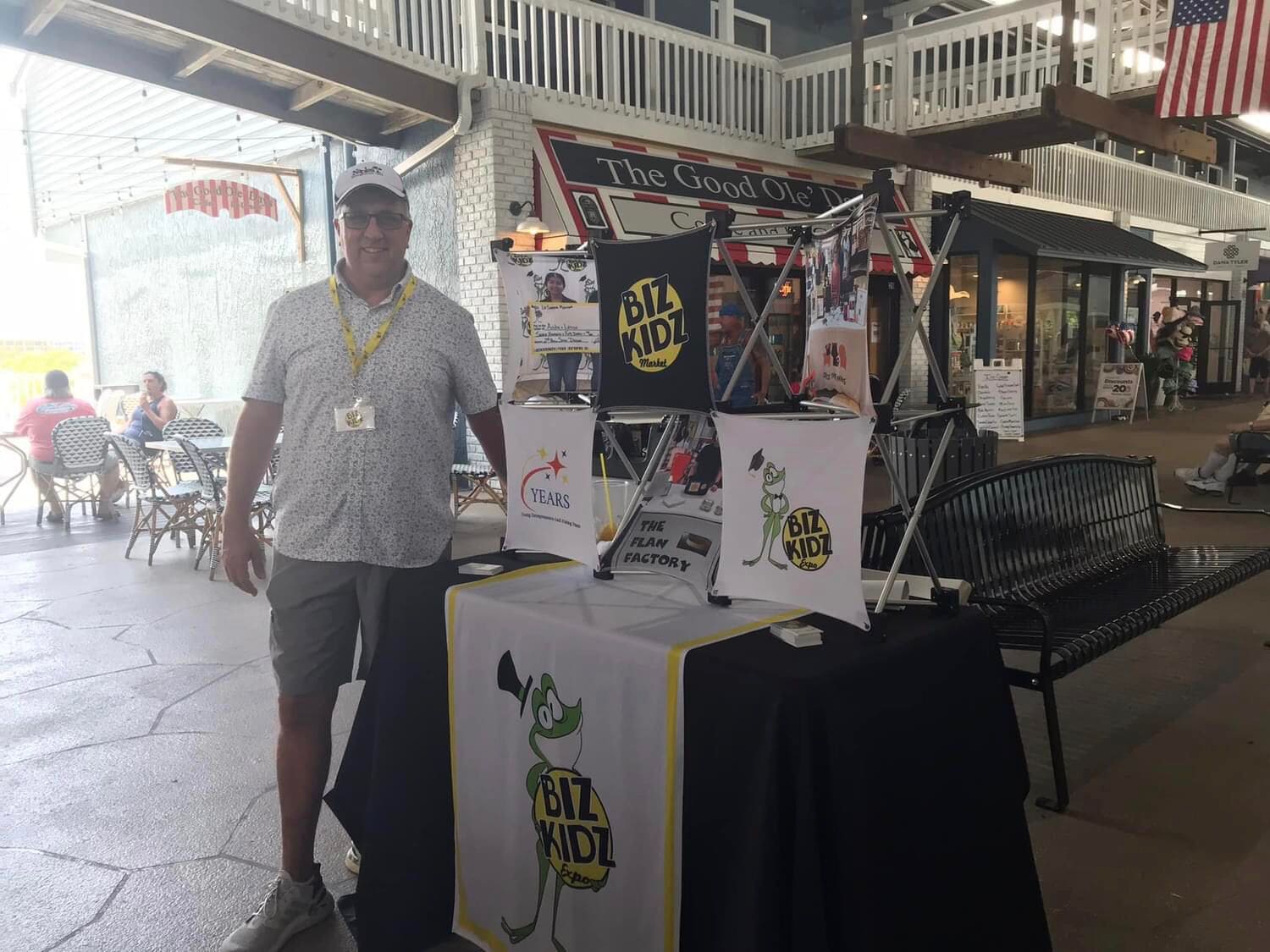 Un hombre está de pie junto a un puesto con un letrero que dice "BIZ KIDDZ Expo".