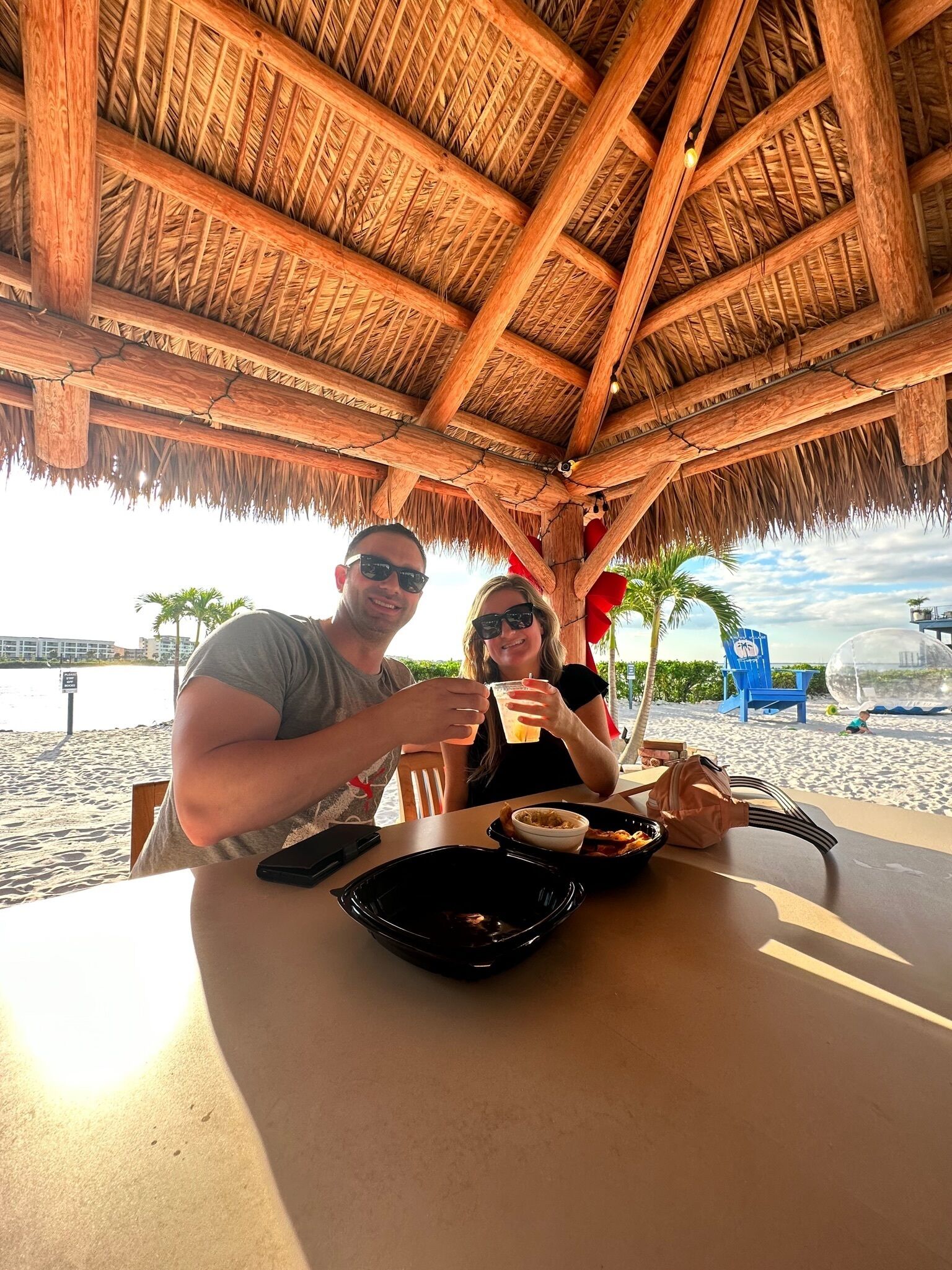 A couple dining at a beachside restaurant with a thatched roof and a view of the sea.