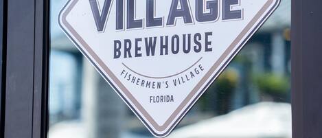 A sign for Village Brewhouse, established in 2018, located in Fishermen's Village, Florida. It is open daily at 11 AM.