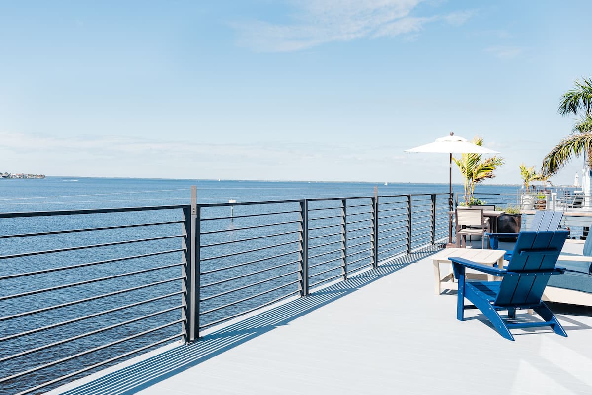 A deck with a railing overlooking a body of water, a table with chairs, and a sun umbrella.
