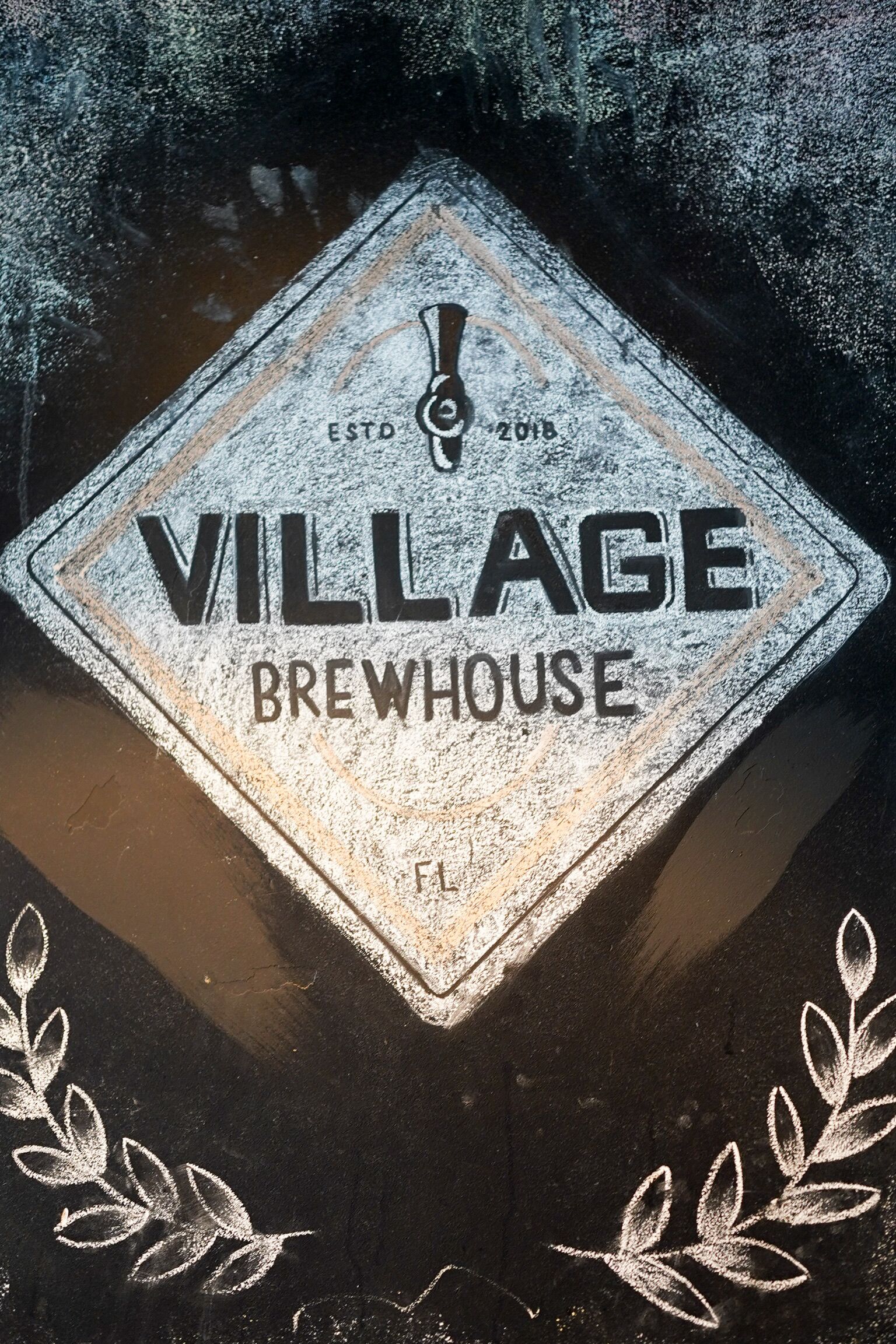 A diamond-shaped sign with "VILLAGE BREWHOUSE" text, established in 2016, and a laurel wreath design at the bottom.