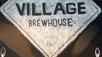 A diamond-shaped sign with "VILLAGE BREWHOUSE" text, established in 2016, and a laurel wreath design at the bottom.